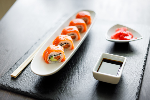 Sushi roll covered with salmon served in long plate on slate board. Traditional japanese food