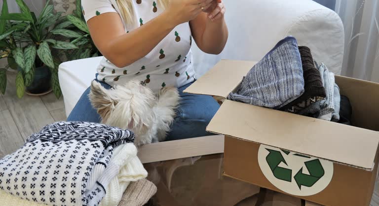 A woman takes pictures of used clothing on her phone, arranging for donation or resale online. A woman and her dog are sorting through old clothes. Reuse clothes, environmentally friendly.