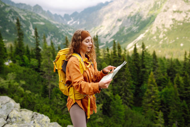 Stylish woman looking at map, exploring woods and mountains.