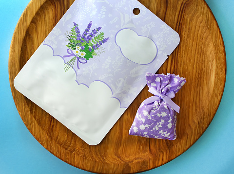 Cosmetics mockup with nourishing sheet mask package on a wooden oak plate with lavender flowers small pouch. Blue background. Top view. Beauty concept.