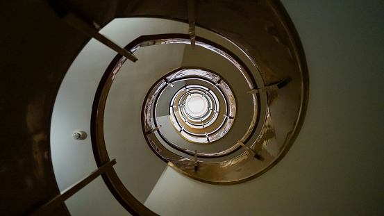 A captivating view from the base of a spiral staircase in a hotel in Funchal, Madeira. Each ascending curve draws the eye toward the light at the top, with the handrails creating a mesmerizing pattern of concentric circles that embody architectural grace.