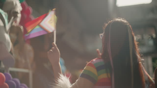 Gay Asian couple hug and show their love with rainbow flags in the street in celebration of LGBTQ+ pride month.