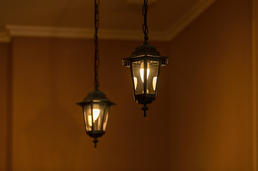 Two hanging lanterns against warm beige walls, one lantern is brighter, creating a cozy illumination.