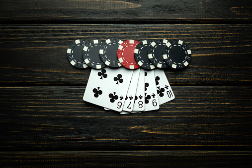 A popular and exciting poker game with a winning straight flush combination. Cards with chips on a dark vintage table in a poker club.