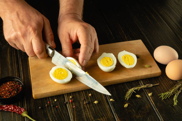 istock Slicing boiled eggs on the kitchen table. A knife in the hand of a chef cuts an egg for preparing breakfast at the cook room 2149412205