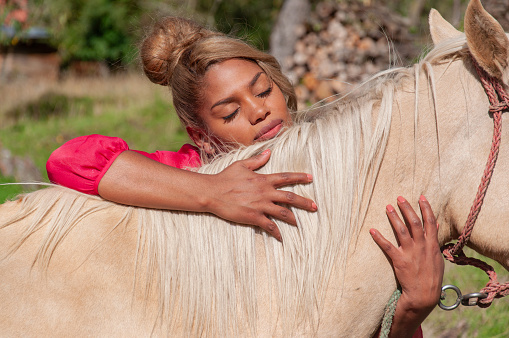 A moment of emotional well-being as a woman tenderly rests her head on a horses back in a peaceful outdoor setting.