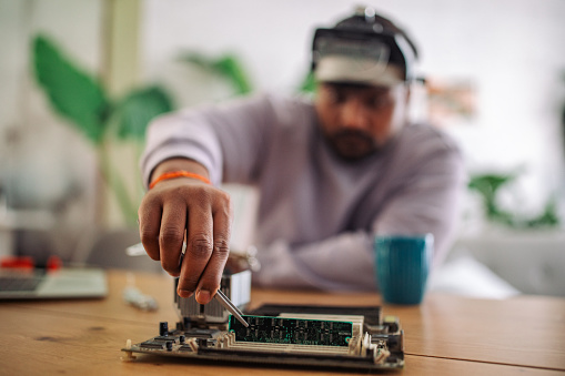 Focused young Indian man working on a circuit board with tools at his home workspace