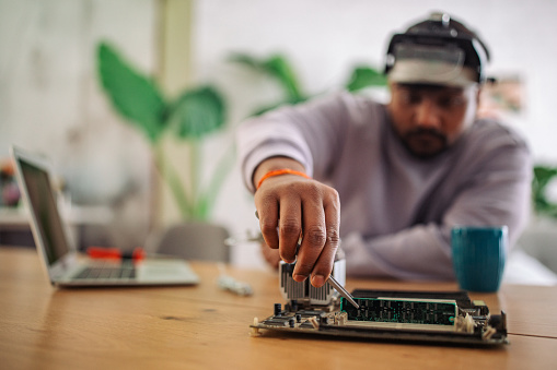 Focused young Indian man working on a circuit board with tools at his home workspace