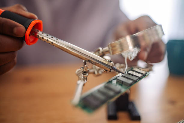 Focused young Indian man working on a circuit board with tools at his home workspace