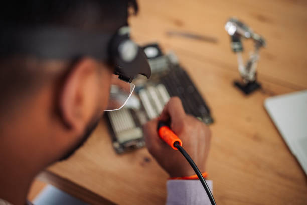 Focused young Indian man working on a circuit board with tools at his home workspace