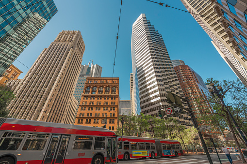 San Francisco, California, April 8, 2024. Red buses traverse below the towering mix of modern and classic architecture in San Francisco.