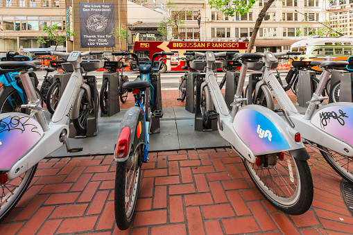 San Francisco, California, April 8, 2024. Rental bikes lined up in San Francisco with a hybrid electric bus in the background.