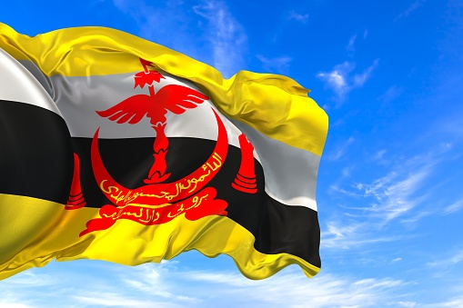 The national flag of Brunei with fabric texture waving in the wind on a blue sky. 3D Illustration