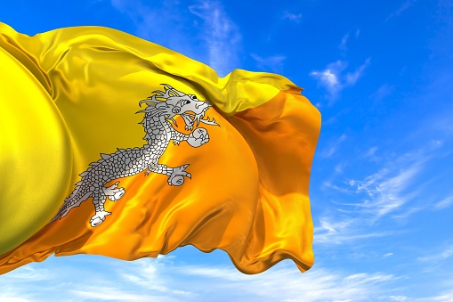 The national flag of Bhutan with fabric texture waving in the wind on a blue sky. 3D Illustration