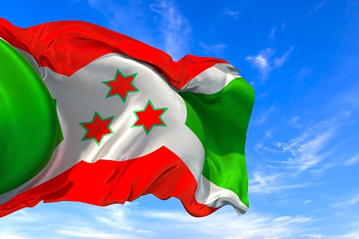 The national flag of Burundi with fabric texture waving in the wind on a blue sky. 3D Illustration