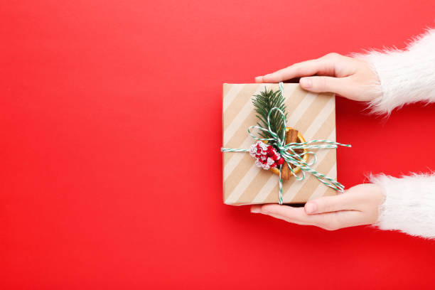 istock Female hands holding gift box on red background 2149421706