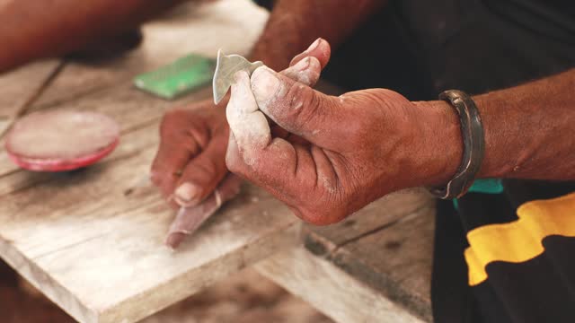 4K video: male hands making dolphin figurines from shells, Indonesia