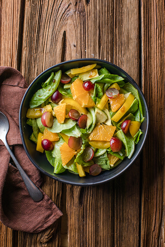 Vegetable salad with pomegranate seeds on a bright metal background, top view. Lettuce, corn salad, cucumber, avocado, orange, pomegranate.