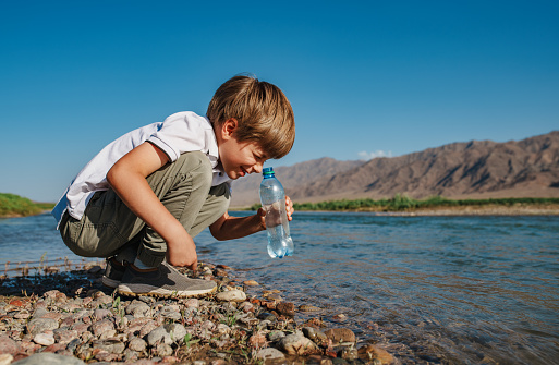 Boy looking into the bottle of water drawn from a mountain river