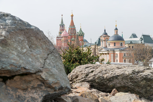 Side view from public park of Church of Barbara on Varvarka, Saint Basil's Cathedral and Spasskaya Tower of Moscow Kremlin over large stones in a spring day. Selective focus. Russian culture theme.