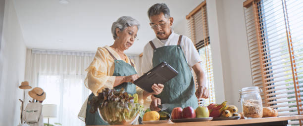 Asian senior adult couple prepare food meal together at home kitchen, use digital tablet for salad dish recipe, cook organic food with fruit, vegetable. Technology people lifestyle, healthy wellbeing una pareja de adultos mayores asiáticos prepara la comida juntos en la cocina de la casa, usa una tableta digital para la receta del plato de ensalada, cocina alimentos orgánicos con frutas y verduras. tecnología, personas, estilo de vida, bienestar sal