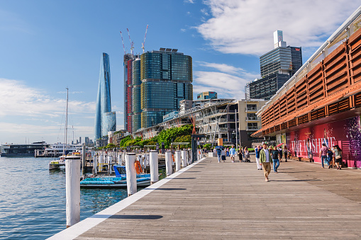 Sydney, Australia - 04 March 2023: Wulugul Walk, a wide promenade on the shores of the Sydney marina with modern buildings, summer sunny day.