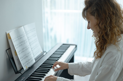 Young woman in white clothes sitting and playing an electronic piano.