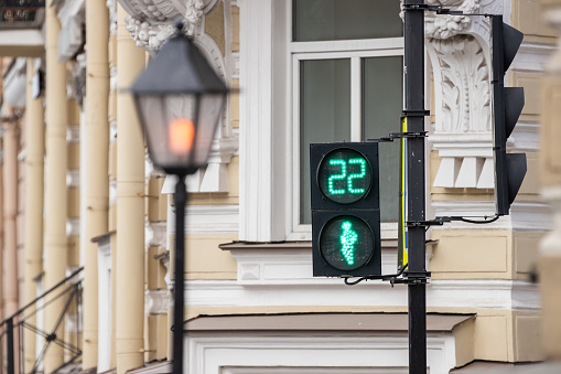 A pedestrian traffic light shows green with a countdown timer against the background of a historical building and an old lantern.