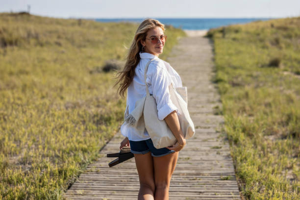 Shot of beautiful young woman walking to the beach while looking at camera