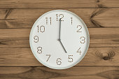 Round white wall clock at 5 o'clock on brown wood background.