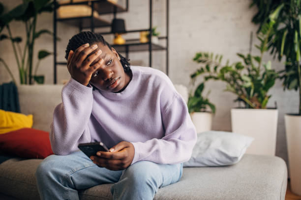 istock Pensive young woman sitting on sofa with smartphone 2149439400