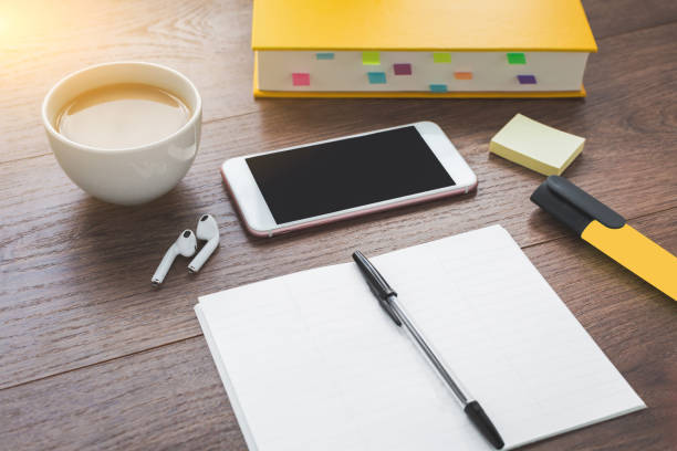 textbook, smartphone, wireless headphones, coffee on a working wooden brown table