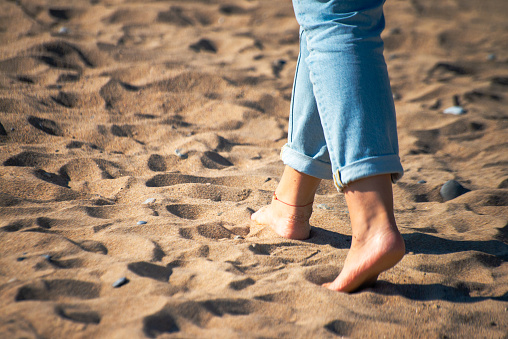 Feel the serene connection with nature as a woman strolls barefoot on the sands, embracing the earth beneath her feet.