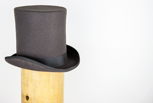 Magic hat. Topper. Elegant vintage gray beige wool felt top hat with black band on the wooden hat block. Grosgrain ribbon trim around rolled brim. Isolated on white background. Close-up. Copy space.