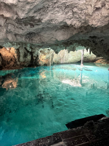 Two women in dresses dining in a mysterious cenote with blue water and limestone walls in an underground cave, Yucatan, Mexico