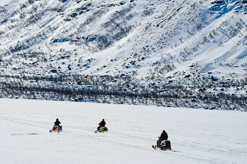 Three snow mobiles making their way on the Lule River in Stora Sjöfallet National Park. It is winter. Snow. Ice.