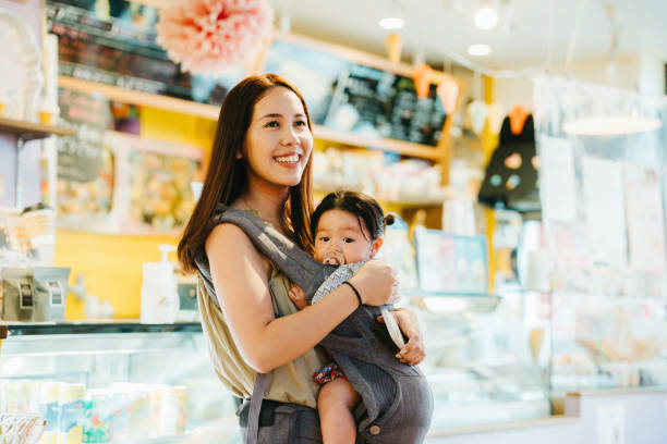 This photo captures a heartwarming moment of an Asian mother cradling her child in a store. The soft lighting and pink floral decor create a cozy atmosphere, reflecting a sense of love and tranquility. Their smiles radiate joy and contentment. esta foto captura un momento conmovedor de una madre asiática acunando a su hijo en una tienda. la iluminación tenue y la decoración floral rosa crean un ambiente acogedor, que refleja una sensación de amor y tranquilidad. sus sonrisas irradian alegrí