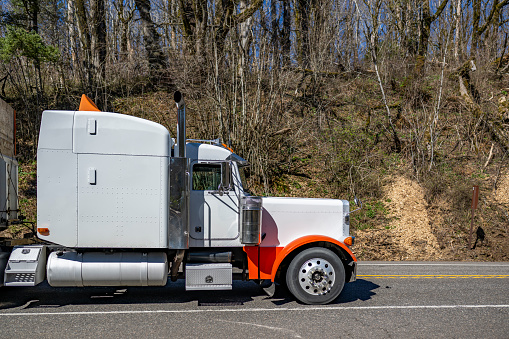 Industrial carrier white big rig semi-truck tractor with extended cab transporting boxes for carry vegetables and fruits on flat bed semi trailer running on the mountain narrow road In Columbia Gorge