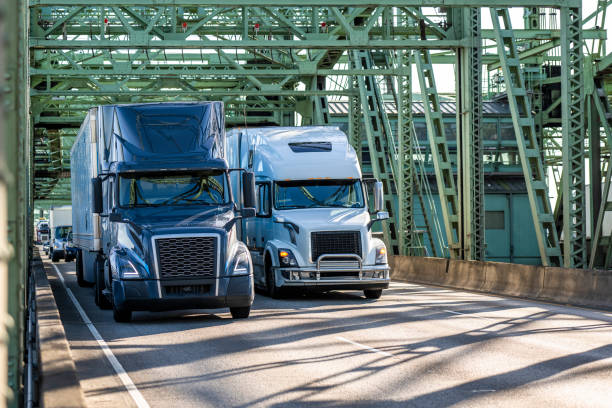 istock Two big rig semi trucks blue and white transporting cargo in dry van semi trailers running side by side on the truss arched bridge 2149466784