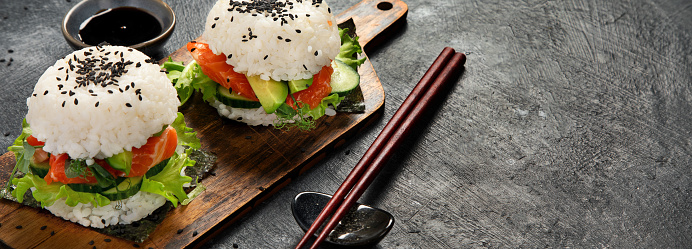 Asian sushi burger, soy sauce, chopstick on dark background. Trendy hybrid food. Copy space, banner