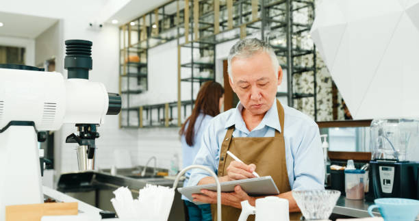istock Senior Asian entrepreneurs man working using a digital tablet to manage orders in modern cafe. Small business owner. 2149476036