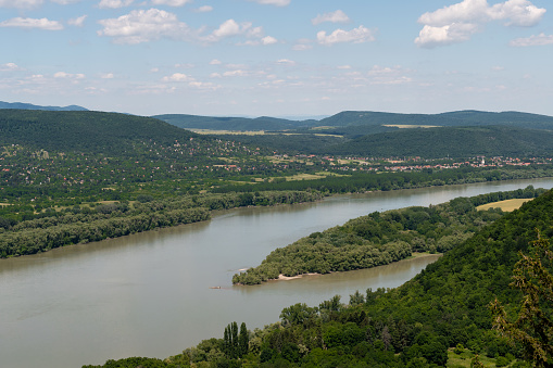View of the Danube, villages and forests with some hills in the background on a sunny day.