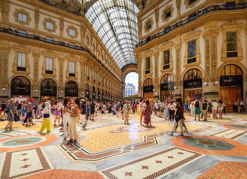 Milan, Italy - June 24, 2023: Interior of the Gallery of Victor Emmanuel II - glass dome, painting at the wall, floors decorated with mosaics. The sights of Milan.