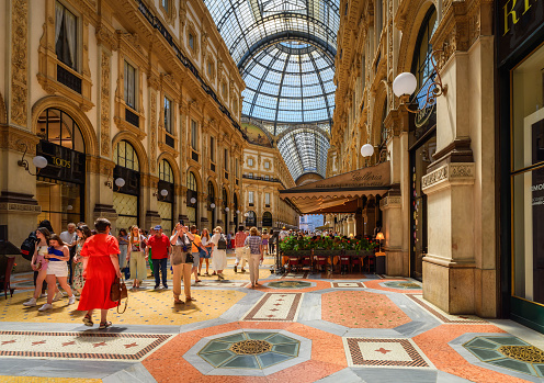 Milan, Italy - June 24, 2023: Interior of the Gallery of Victor Emmanuel II - glass dome, painting at the wall, floors decorated with mosaics. The sights of Milan.