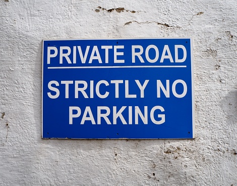 UK no parking roadsign. White font on blue background against an aged white plastered wall