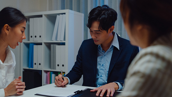 Young Asian businessman mentor corporate leader manager counselor communicate with businesswoman and sign a contract at office night. Businesspeople in workplace concept.