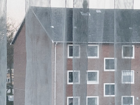Gazing through a white-curtained window at a Copenhagen apartment building