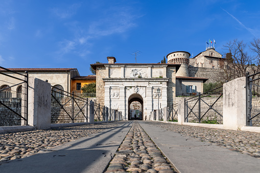The perspective from ground level leads through a cobbled pathway to Brescia castle entrance, where a lion relief proudly marks the historical gateway
