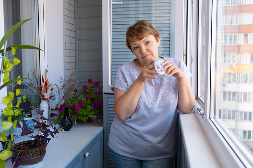 An attractive elderly woman drinks coffee on the balcony. Enjoying life