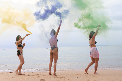 Joyful of Asian lady friends wearing bikini playing color smoke on the beach, Summer holiday and relaxing concept, summer holiday on a tropical beach